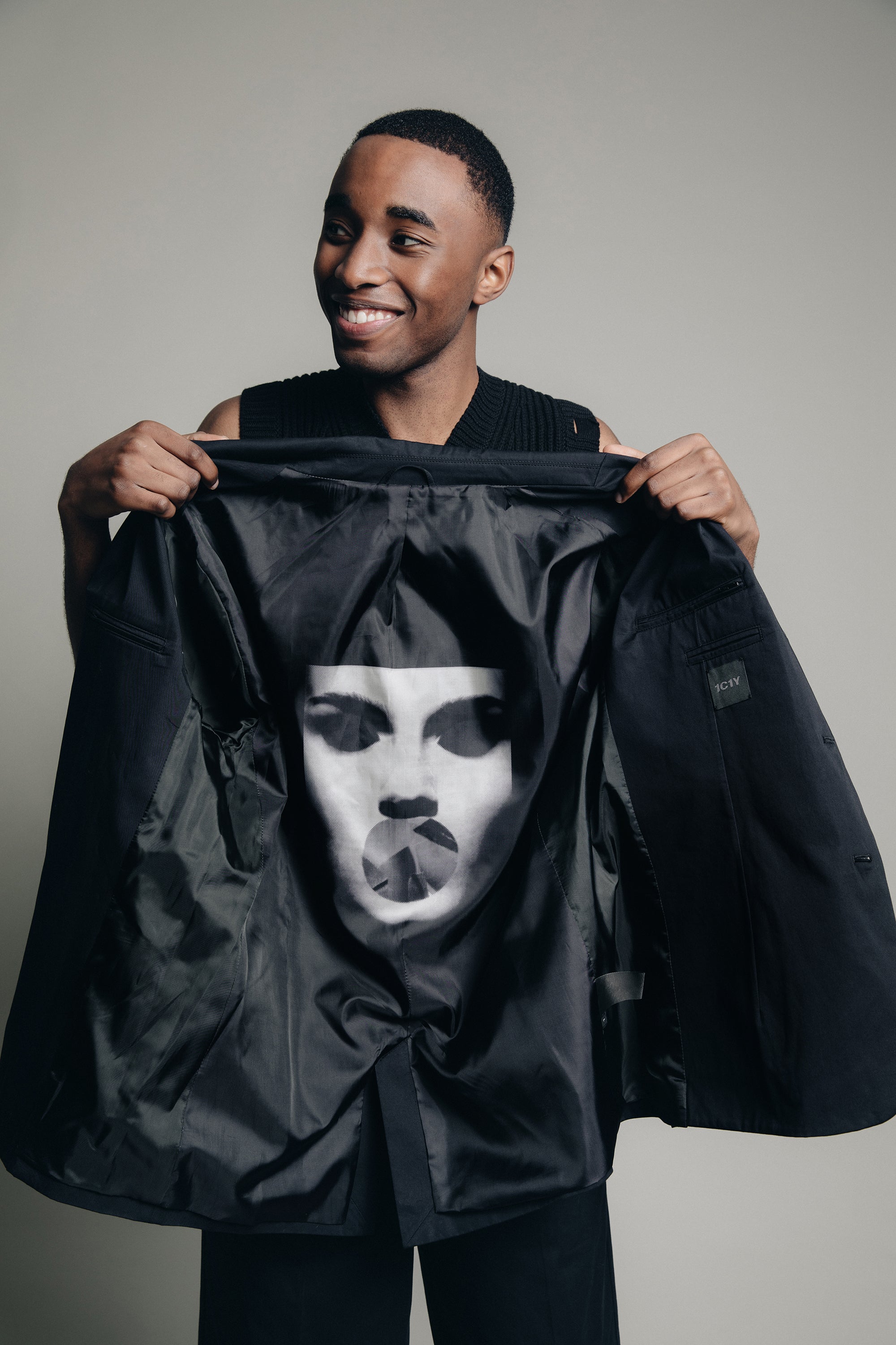 Detail shot of model in studio wearing 1c1y ss23 andr1a black blazer jacket showing white face print in lining