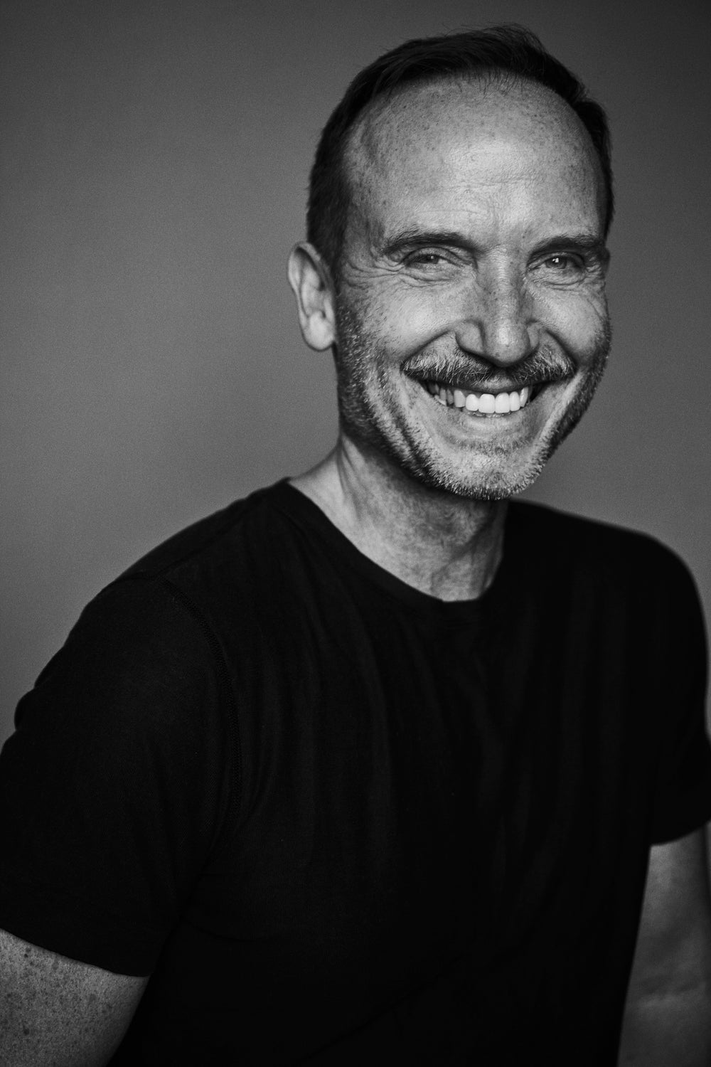 black and white portrait of Bernd keller smiling taken by Stefan Rappo he is wearing a black tshirt