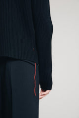 Detail web shop picture from back of male model wearing w1ad slim ribbed merino sweater with thumbholes showing red stitching and garn hanging down before clean studio background 1c1y