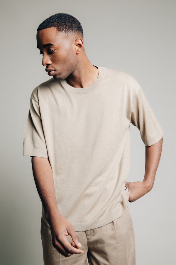 Detail shot of model in studio wearing 1c1y ss23 1van superfine merino t shirt in sand colours grabbing in back pocket showing wavy texture of the fabric